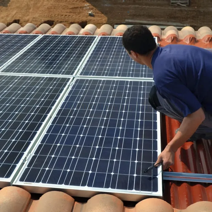 Un poseur installe des panneaux solaires sur une toiture en tuiles