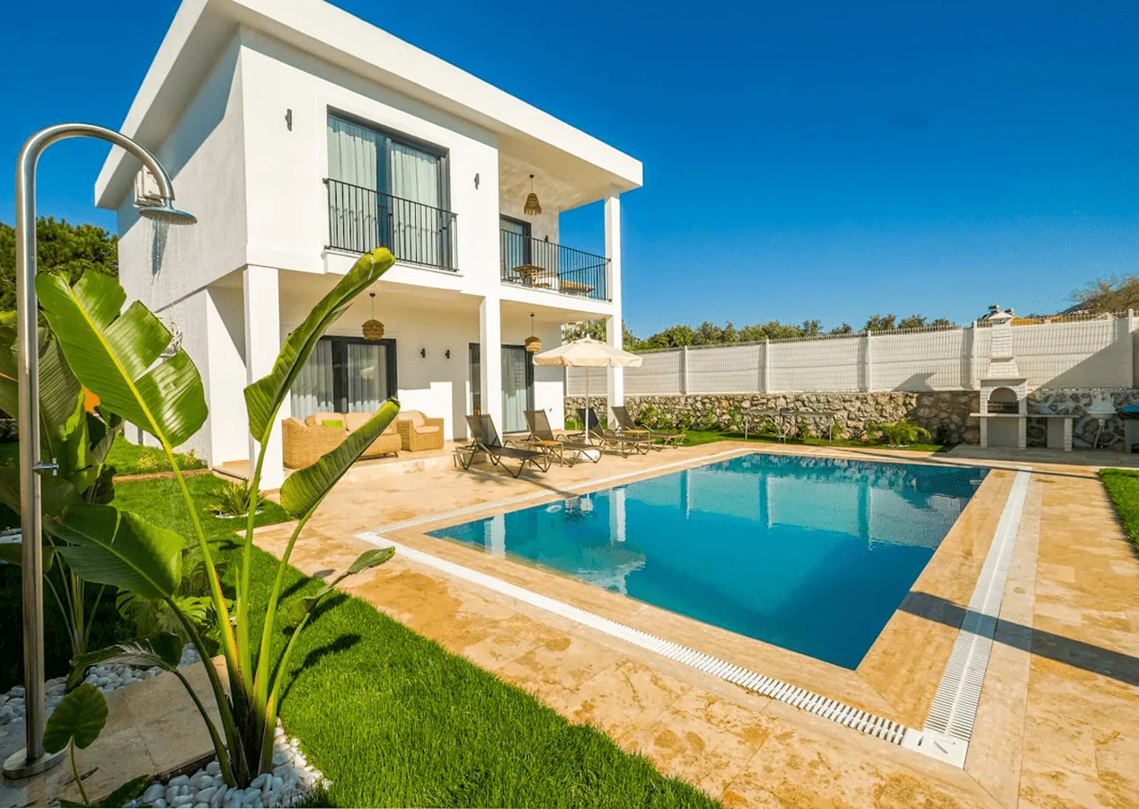 Piscine enterrée devant une villa blanche, plage en pierre et palmier