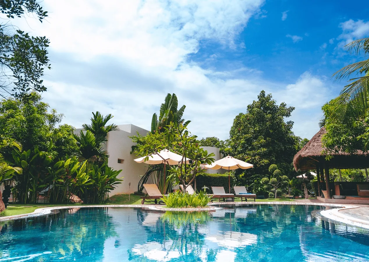 Grande piscine d'hôtel entourée de palmiers et de parasols