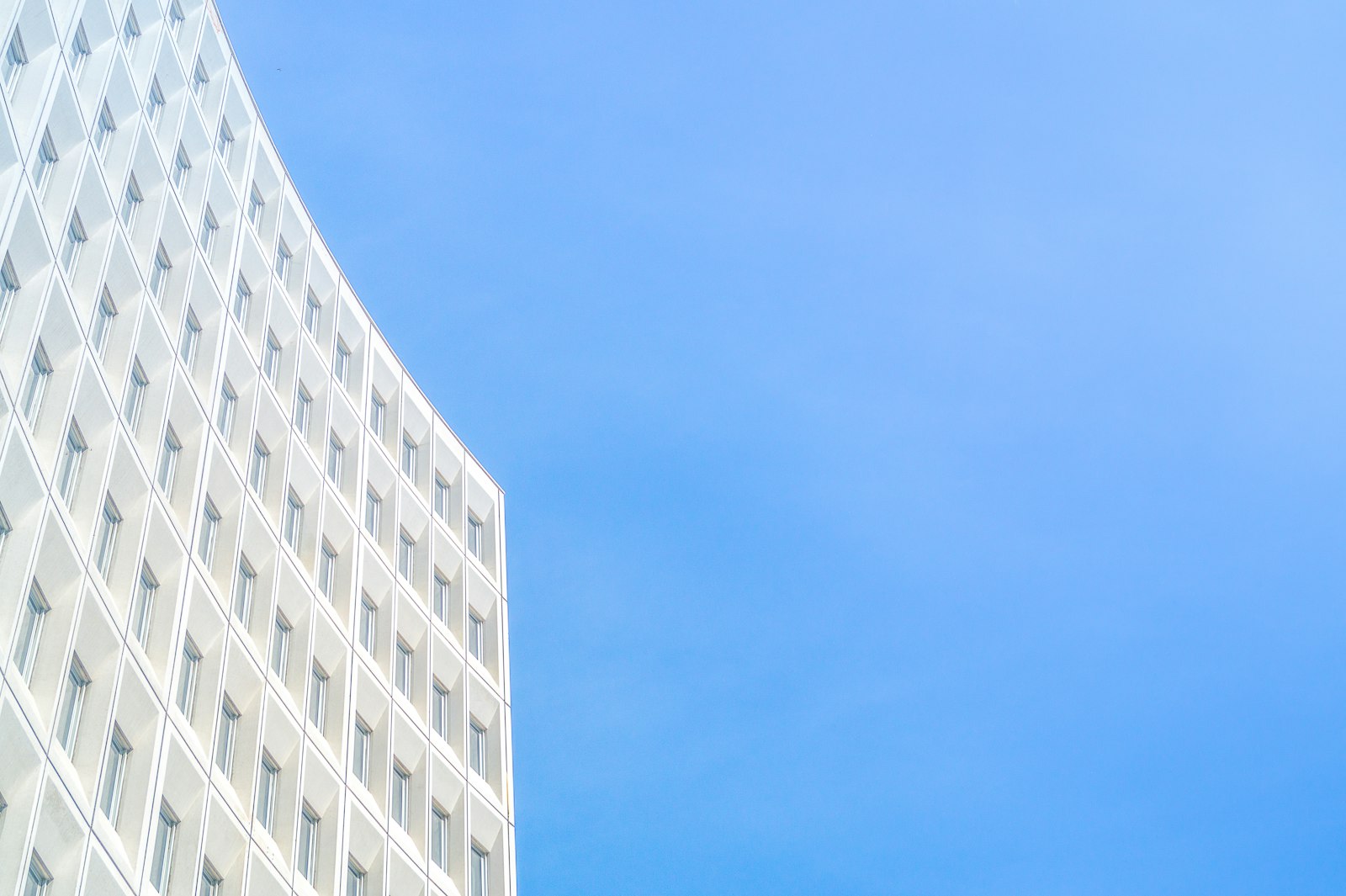 Façade courbe d’un immeuble de bureaux, résille blanche sur ciel bleu